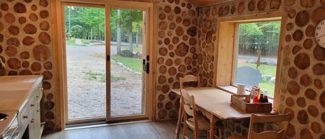 A rustic room with a stone wall, a wooden table with chairs, a window, and a kitchen area with a stove.