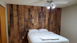 Un dormitorio con paneles de madera, una cama con ropa blanca y un ventilador de techo.