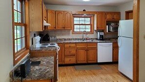Una cocina con gabinetes de madera, encimera de granito, horno empotrado, lavavajillas y refrigerador.