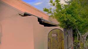 A building with a number 505 sign on a wooden door, a concrete pathway, and a tree with green leaves.