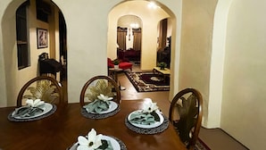 A dining area with a wooden table set for six, surrounded by chairs. There is a carpeted floor and a doorway leading to another room.