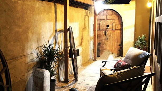 A cozy outdoor seating area with a wooden bench and a table, surrounded by stone walls and a rustic wooden door.