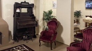 A living room with a grand piano, two red velvet armchairs, a patterned rug, and a television mounted on the wall.