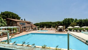 A swimming pool area with lounge chairs and umbrellas, surrounded by buildings and trees. - Two-room apartment for 4 people, 36 m2, consisting of:Living area with kitchenette (4 burners) and 2 single beds, double bedroom,bathroom with shower, covered terrace equipped with table, chairs and two deck chairs. (Guardistallo)