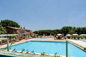 A swimming pool area with lounge chairs and umbrellas, surrounded by buildings and trees. - Two-room apartment for 4 people, 36 m2, consisting of:Living area with kitchenette (4 burners) and 2 single beds, double bedroom,bathroom with shower, covered terrace equipped with table, chairs and two deck chairs. (Guardistallo)