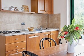 A kitchen with wooden cabinets, a granite countertop, a gas stove, and a dining table with chairs.
