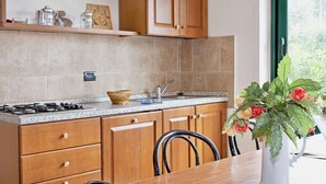 A kitchen with wooden cabinets, a granite countertop, a gas stove, and a dining table with chairs. - Two-room apartment for 4 people, 36 m2, consisting of:Living area with kitchenette (4 burners) and 2 single beds, double bedroom,bathroom with shower, covered terrace equipped with table, chairs and two deck chairs. (Guardistallo)