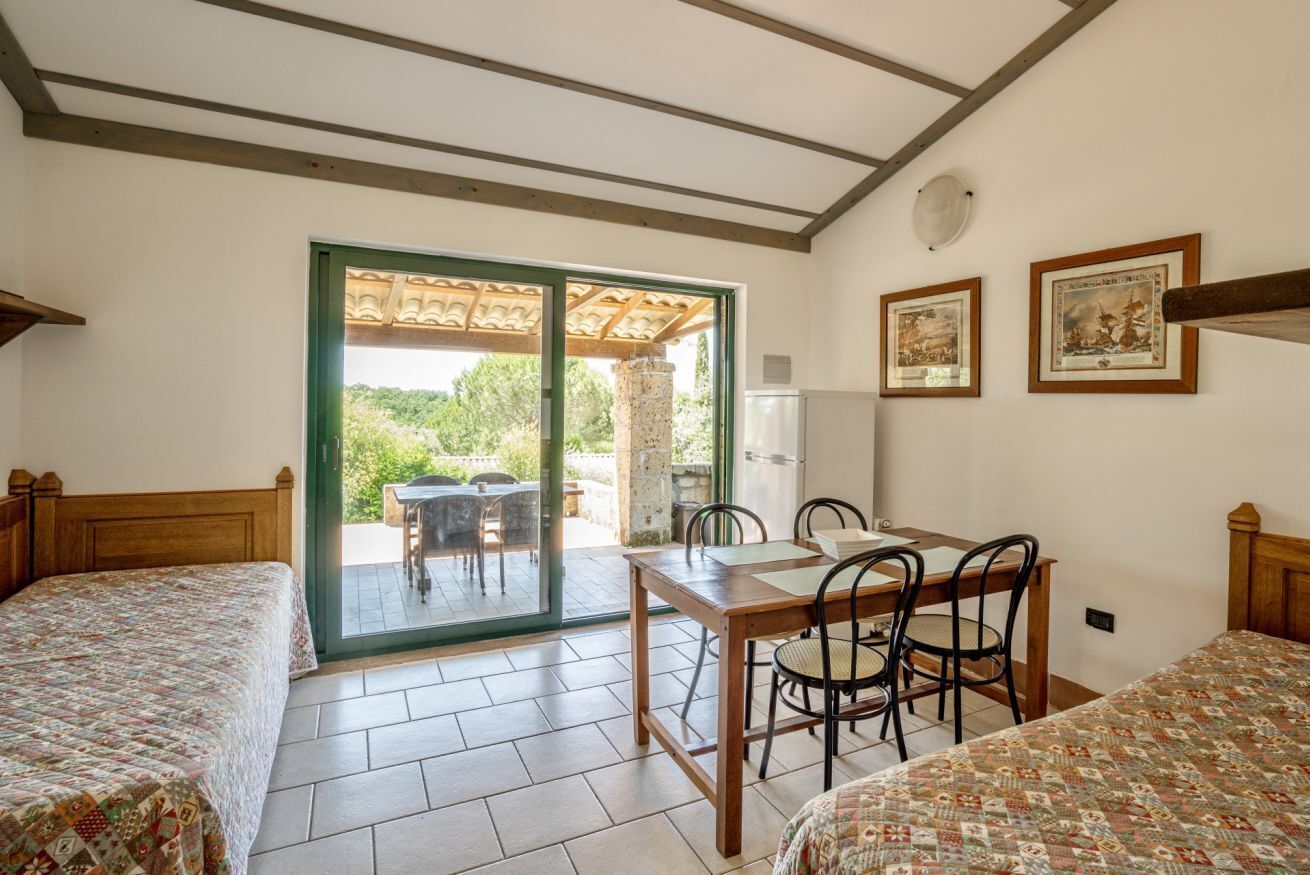 A bedroom with two beds, a dining table with chairs, a sliding glass door to a patio, and framed pictures on the wall.