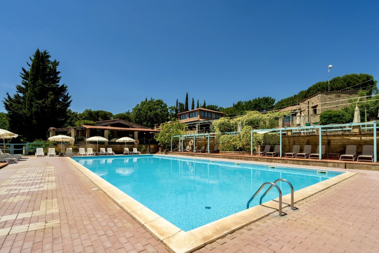 Une piscine entourée d’arbres et d’immeubles, avec des chaises longues et des parasols.