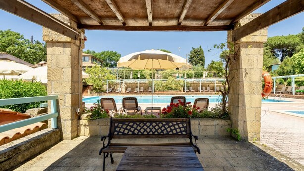 A wooden pergola with a bench overlooking a swimming pool area. - Two-room apartment for 4 people, 36 m2, consisting of:Living area with kitchenette (4 burners) and 2 single beds, double bedroom,bathroom with shower, covered terrace equipped with table, chairs and two deck chairs. (Guardistallo)