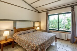A bedroom with a bed, two bedside lamps, a window with curtains, and a radiator.