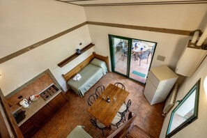 A compact kitchen with a dining area, a bench, and a view to an outdoor patio. - Two-room apartment for 5 people, 50 m2, consisting of:Living area with kitchenette (4 burners) and 2 single beds, separate area with a single bed, double bedroom, bathroom with shower, covered terrace equipped with table, chairs and two deck chairs. (Guardistallo)
