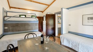 Ein kleines Zimmer mit einem Etagenbett, einem Esstisch, zwei Weingläsern und einem Stuhl.