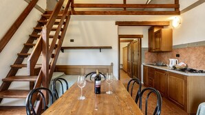 Eine Holztreppe führt zu einem Schlafzimmer auf dem Dachboden, einem Essbereich mit einem Holztisch und vier Stühlen sowie einer Küche mit Holdekor-Schränken und einer Arbeitsplatte.
