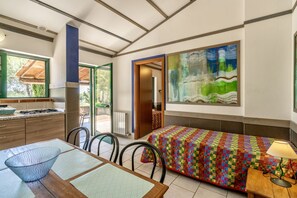 A modern kitchen with a dining area, a colorful quilted bed, and a large abstract painting on the wall.