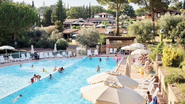 Ein Schwimmbecken, umgeben von Liegestühlen und Sonnenschirmen, mit badenden und entspannenden Personen.