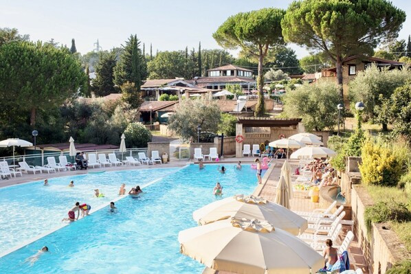 A swimming pool surrounded by lounge chairs and umbrellas, with people swimming and relaxing.