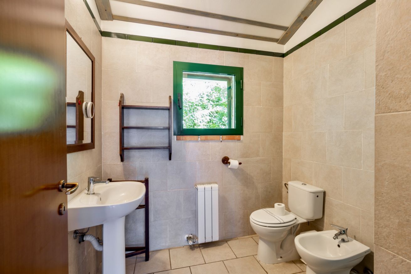 Un bany amb rentapla, vàter, bidet i una finestra amb marc verd.
