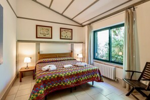 A bedroom with a large bed, two bedside lamps, a wooden headboard, a window with curtains, and a radiator.