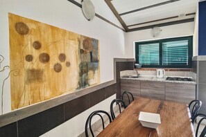A modern kitchen with a large abstract painting, a dining table with chairs, and a window with blinds.