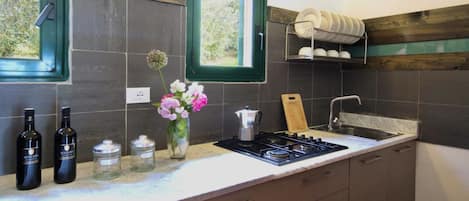 A kitchen with dark tiles, a window, a stove, a sink, and a shelf with dishes.