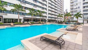 A modern hotel with a large outdoor swimming pool surrounded by lounge chairs and palm trees. - Departamento en Puerto Santa Ana (Guayaquil)