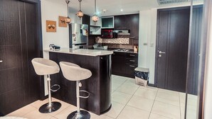 A modern kitchen with dark cabinetry, a central island with bar stools, a microwave, and a refrigerator. - Departamento en Puerto Santa Ana (Guayaquil)