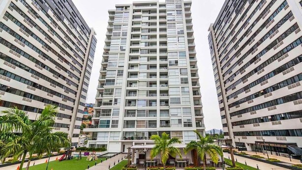 A high-rise residential building with multiple balconies, a central courtyard with palm trees, and a modern architectural design. - Departamento en Puerto Santa Ana (Guayaquil)