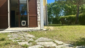 A stone building with a wooden door and shutters, a stone pathway, and a grassy area with a bench. - M368 - Marcelli, new three-room apartment with garden (Marcelli)
