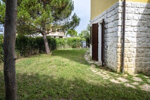 A stone building with a door and a small garden area with grass and a tree.