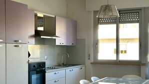 A modern kitchen with a stove, sink, and cabinets, a dining table with chairs, and a window with blinds. - P013 - Porto Recanati, renovated three-room apartment 50 meters from the sea (Porto Recanati)