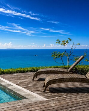 Terraza de madera con sillones de mimbre que dan a una piscina y el océano.