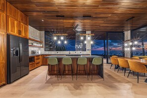 A modern kitchen with wooden cabinets, a stainless steel refrigerator, a bar area with stools, and a large island with bar stools.