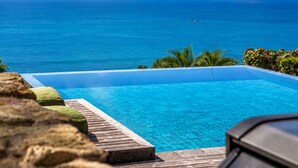Kirkas, sininen taivas, tyyni meri ja uima-allas, jonka yhteydessä on puinen terassi.
