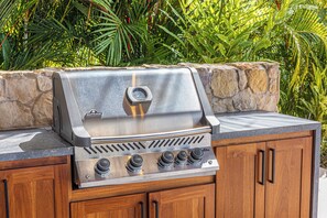 A stainless steel Napoleon grill with four knobs, set on a wooden cabinet with a stone backdrop.