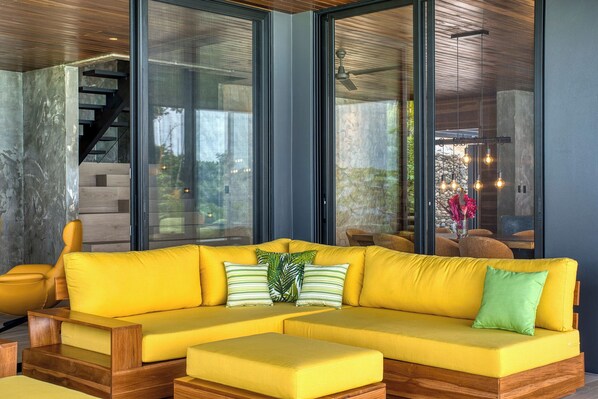 A modern living room with a yellow sectional sofa, wooden coffee table, and a staircase leading to an upper level.