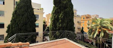 A rooftop terrace with terracotta tiles, metal railings, and tall cypress trees.