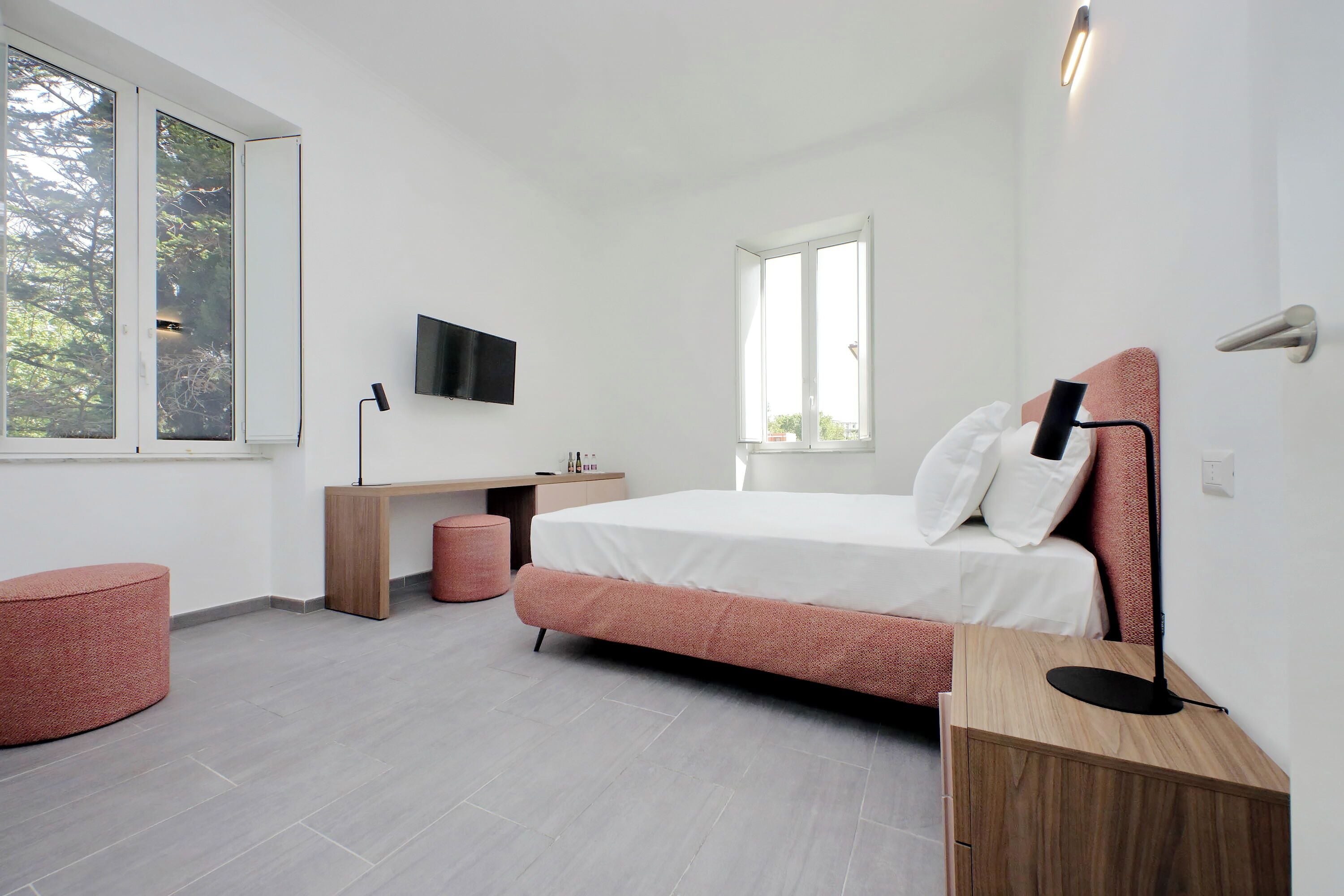 Quarto moderno com cama, escrivaninha e cadeira, TV montada na parede e janela que oferece luz natural.