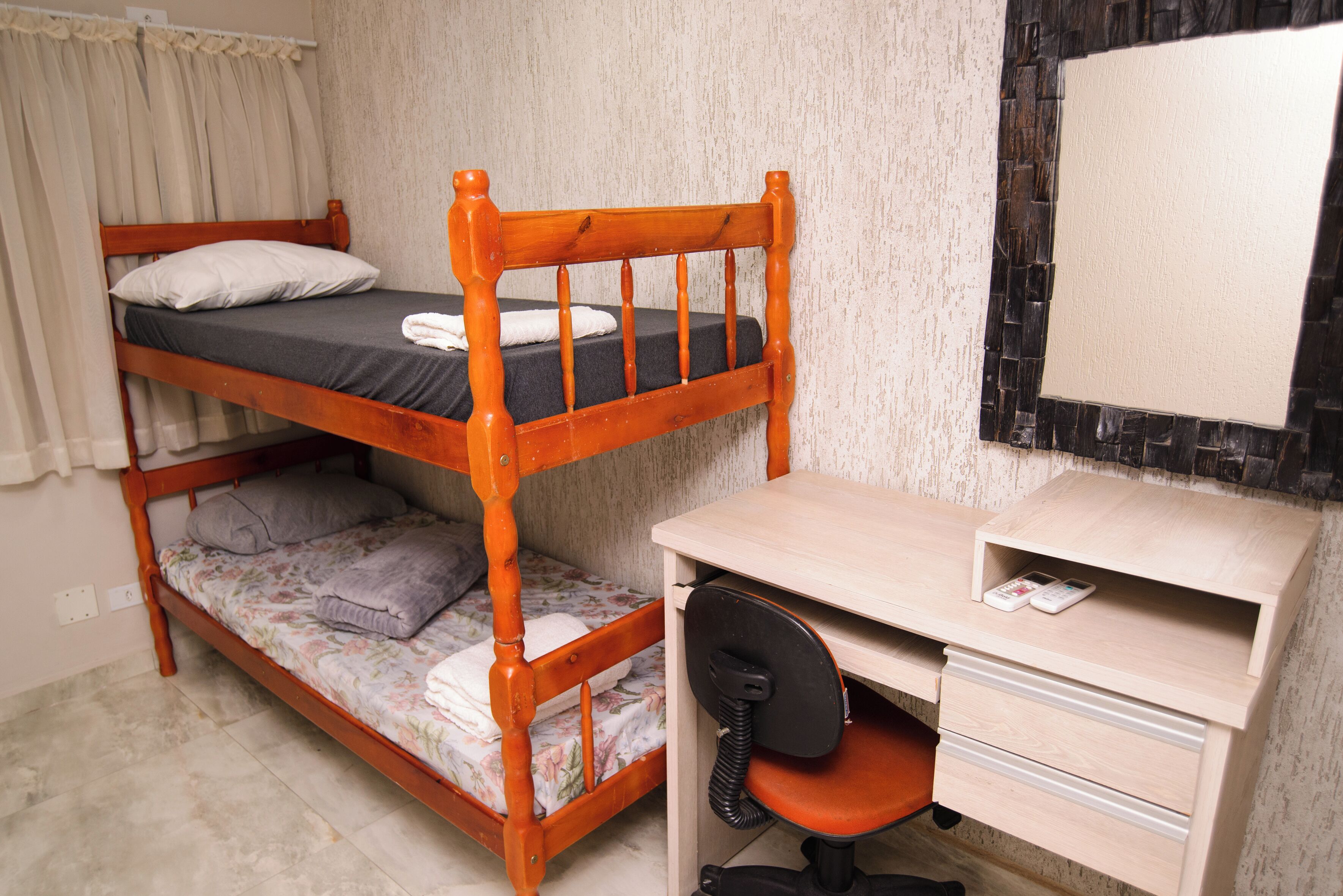 Un letto a castello con una scrivania, una sedia, uno specchio e una piccola mensola con un telefono.