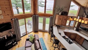 A spacious living area with a large window, a sofa, and a television. - Lake front cottage less than 20 min from golf simulator/pool/bar/grill (Arkdale)