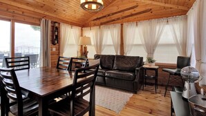 A wooden-paneled room with a dining table, chairs, a sofa, and a small side table with a lamp. - Lake front cottage less than 20 min from golf simulator/pool/bar/grill (Arkdale)