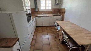 Een kleine keuken met witte kastjes, een houten aanrechtblad en een raam met gordijnen.