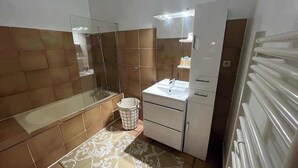 Een badkamer met een douchecabine van glas, een wastafel met spiegel en een betegelde vloer.
