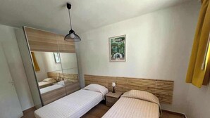 Een slaapkamer met twee bedden, een spiegel, een poster en een hanglamp.