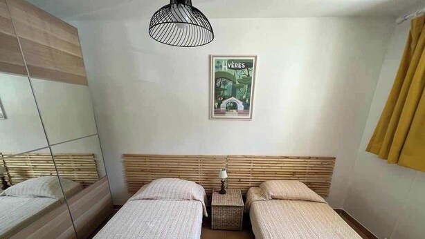 Een kamer met twee eenpersoonsbedden, een klein tafeltje met een lamp, een poster aan de muur en een spiegel aan de linker muur.