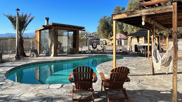 A pool area with two wooden Adirondack chairs, a glass-enclosed structure, and a pergola. - Private ranch getaway perfect for stargazing, relaxing pool desert hot bsprings  (Desert Hot Springs)
