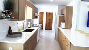 A modern kitchen with wooden cabinets, a white countertop, a sink, and a microwave.