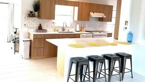 A modern kitchen with wooden cabinets, a large island with stools, and a view of the living area.