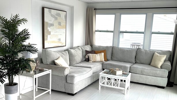 A modern living room with a grey sectional sofa, a white coffee table, a potted plant, and a ceiling fan.