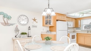 Una cocina moderna con armarios de madera, una mesa redonda de vidrio, sillas blancas y un ventilador de techo.